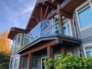 Photo of the exterior of a home with a second floor deck featuring frameless glass railings. 