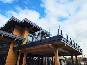 a black and wood building with a frameless glass railing against a bright blue sky