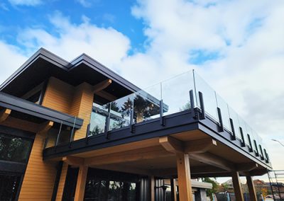 a black and wood building with a frameless glass railing against a bright blue sky
